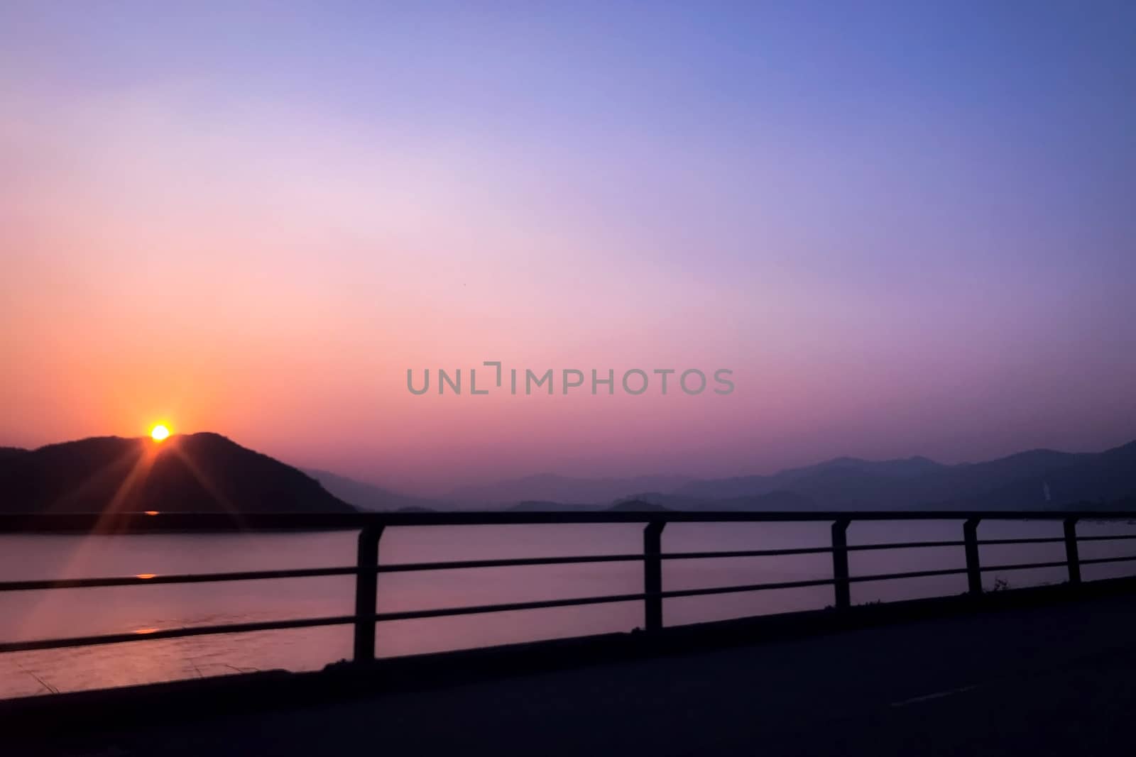 The silhouette of fence, mountain, ocean and sun at sunset