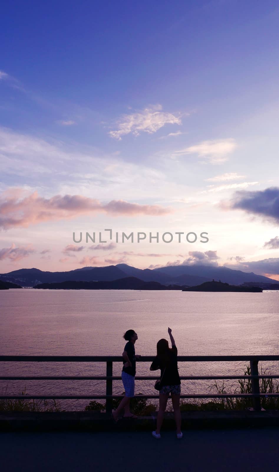 two people, mountain, footpath fence and the sea at sunset