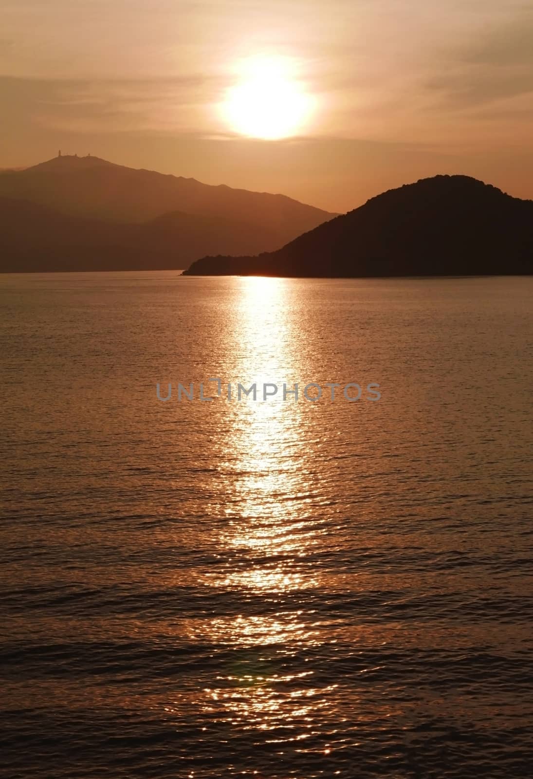 Vertical sun, mountain, ocean and water wave at sunset