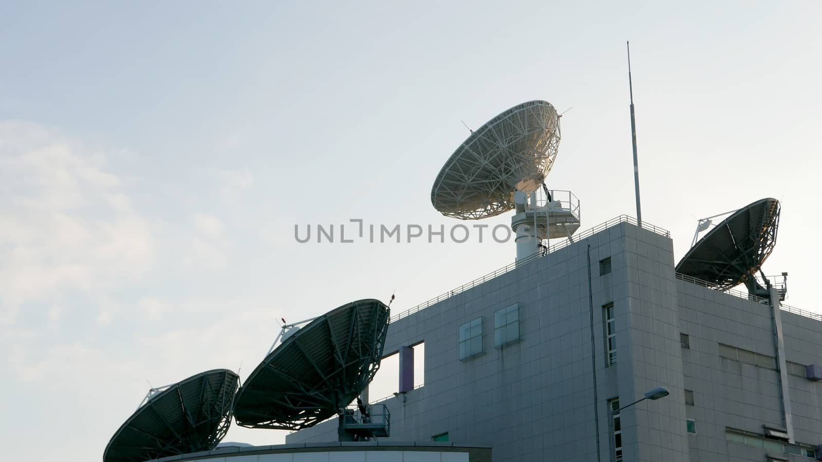 Few satellite dishes on roof top building with the blue sky by cougarsan