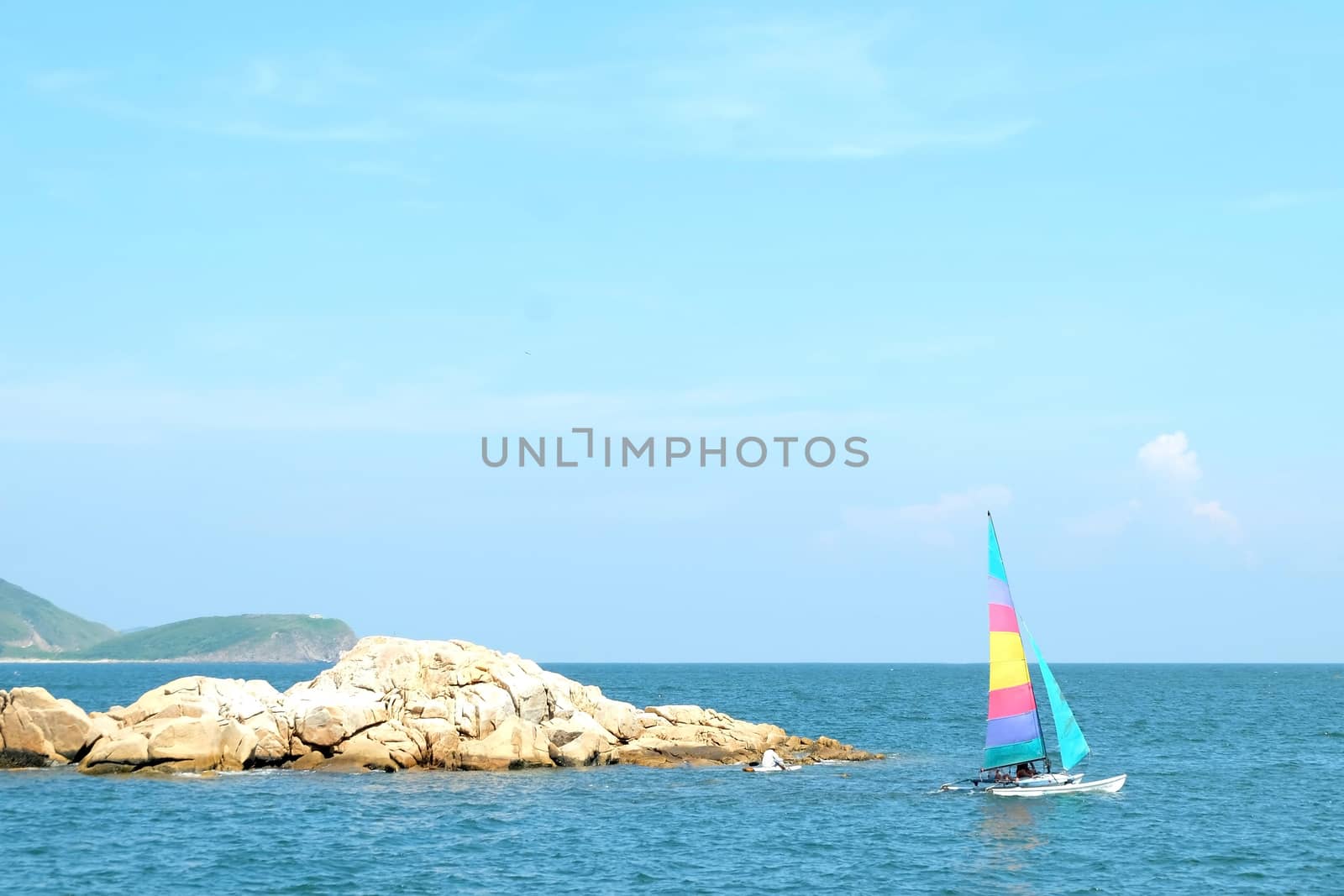 Colorful sailboat passes the small rock island in the sea