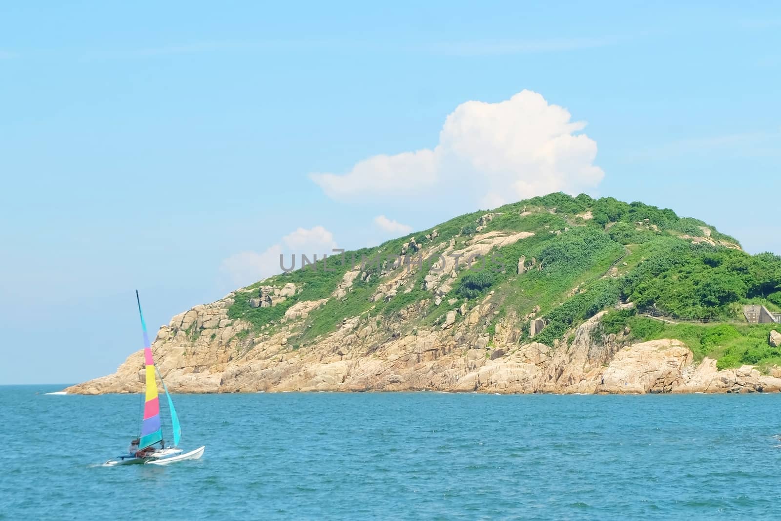 Colorful sailboat passes the small rock island in the sea