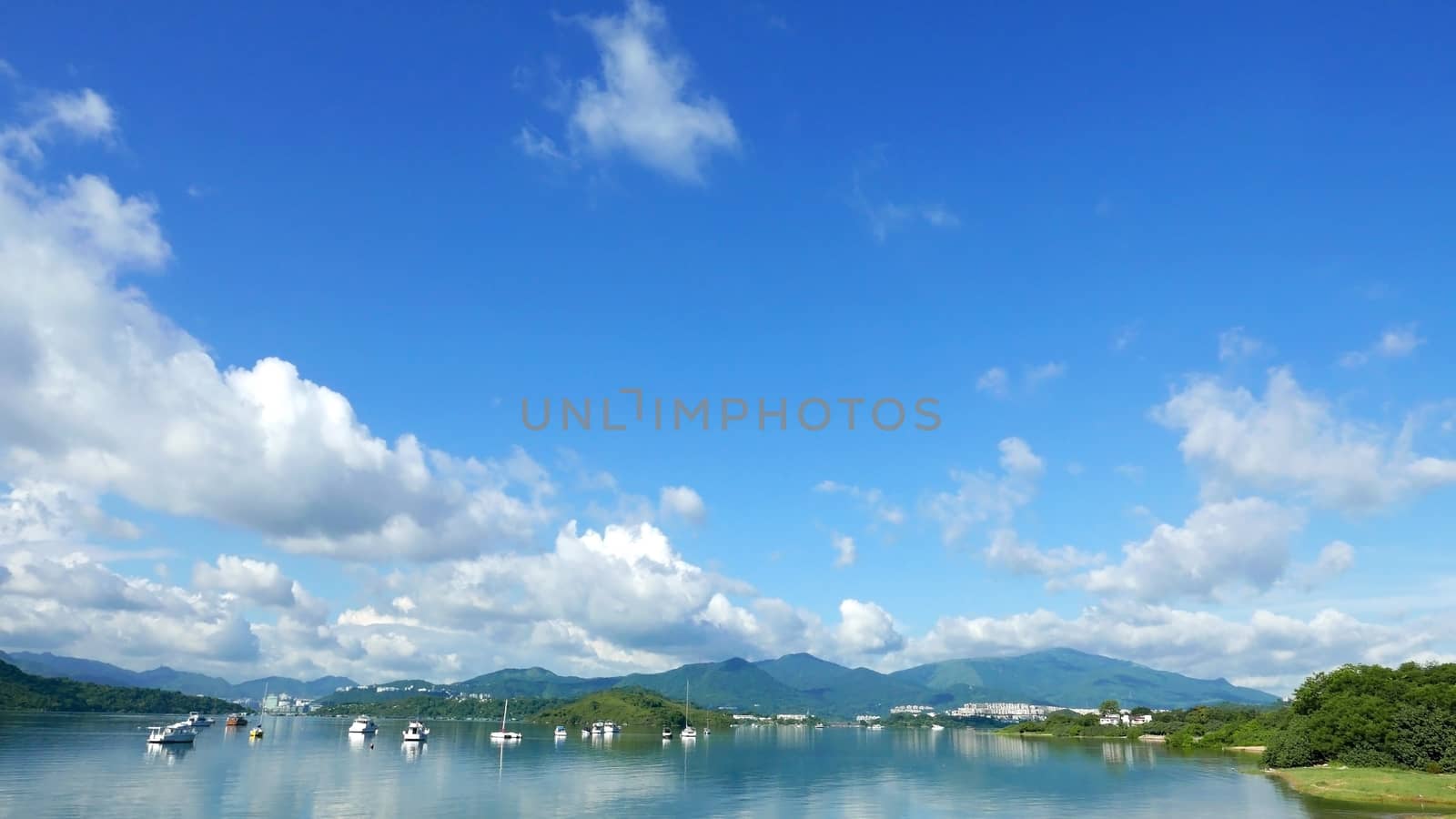 Boats, white clouds, lake and blue sky with reflection shadow by cougarsan