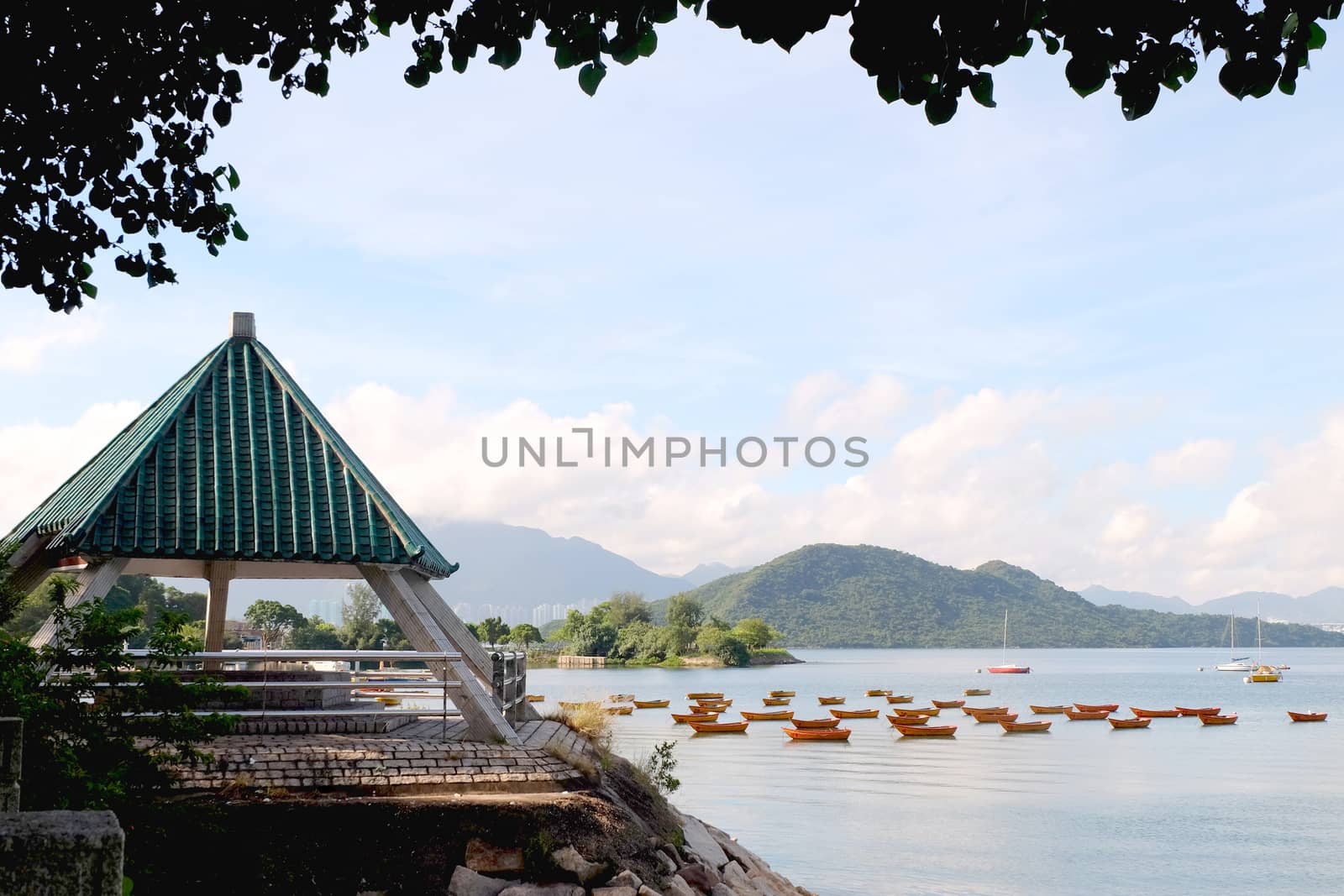 The mountain, recreational wooden boats, clouds, lake, blue sky and sun in Hong Kong