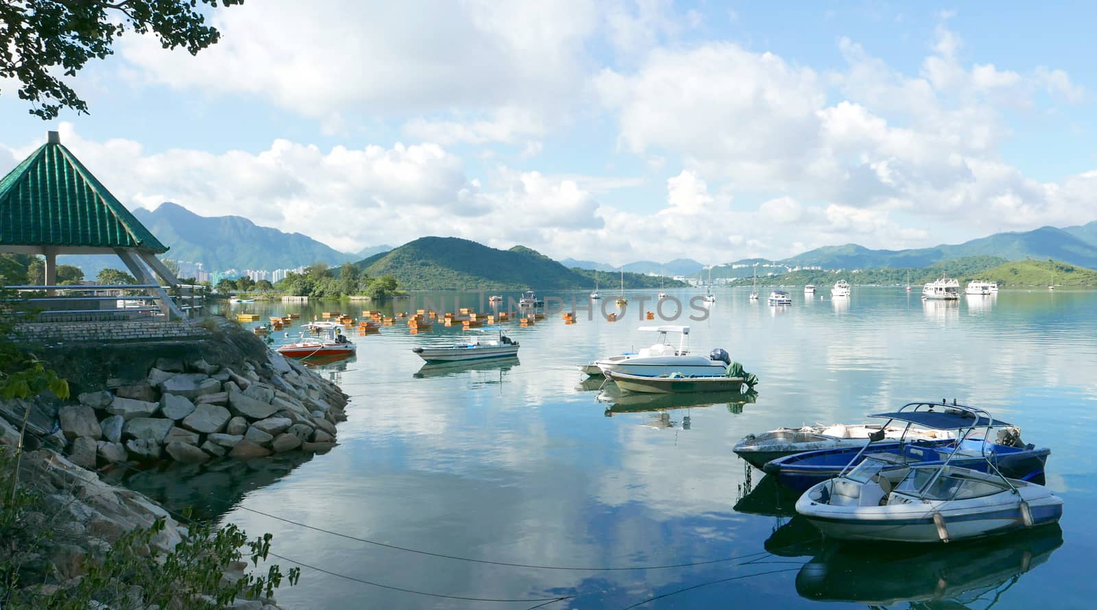 The mountain, recreational wooden boats, clouds, lake, blue sky and sun in Hong Kong