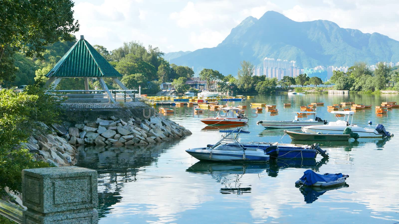 The mountain, recreational wooden boats, clouds, lake, blue sky and sun in Hong Kong