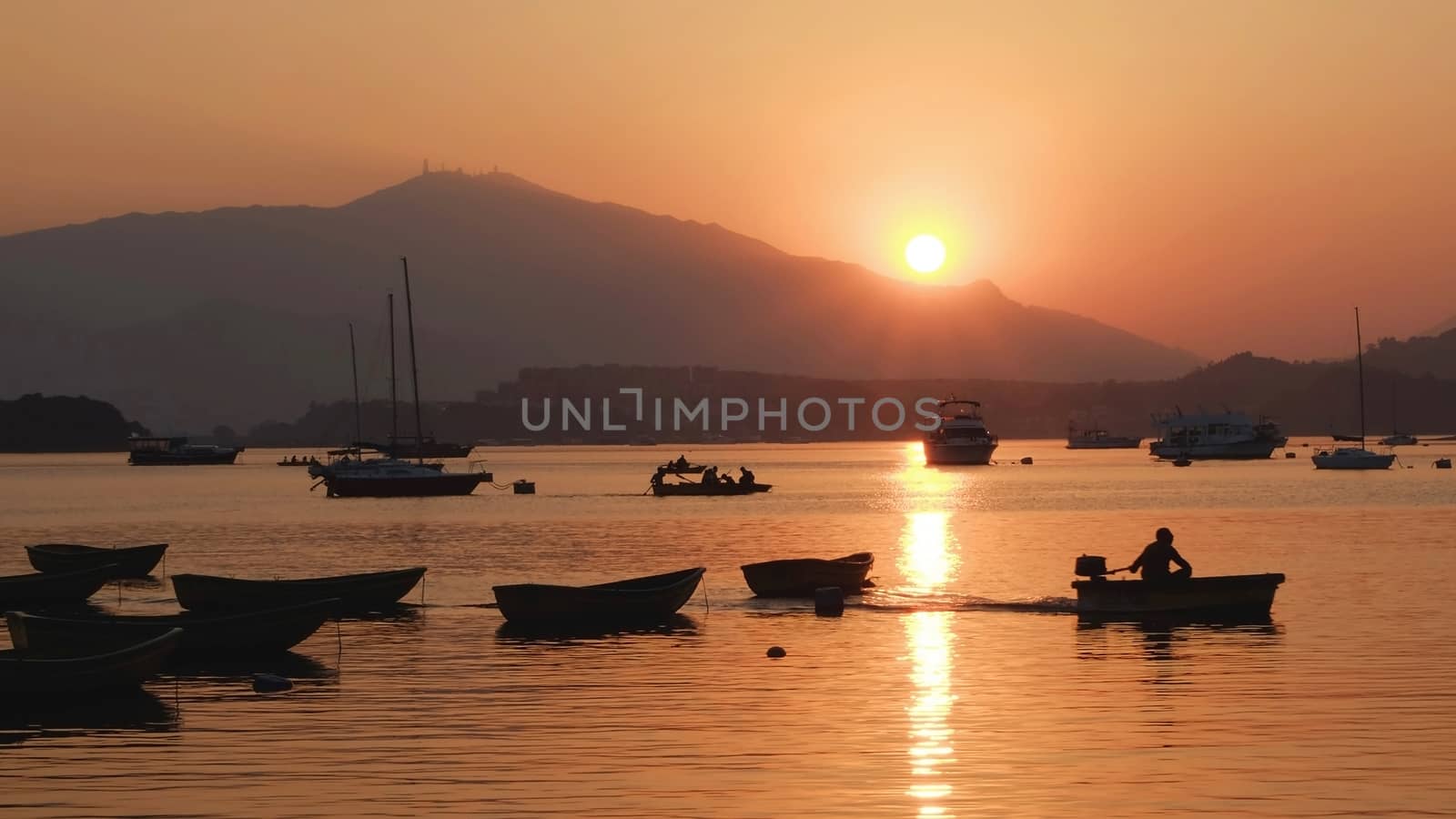 The silhouette of fishing boat on lake with sun and mountain at sunset