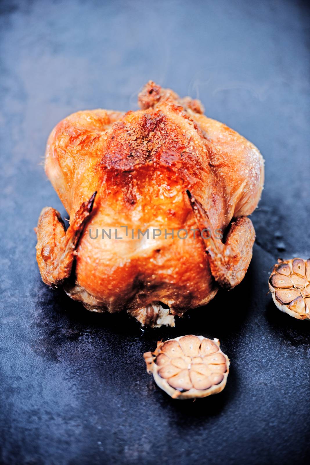 Whole oven roasted chicken with garlic on stone surface