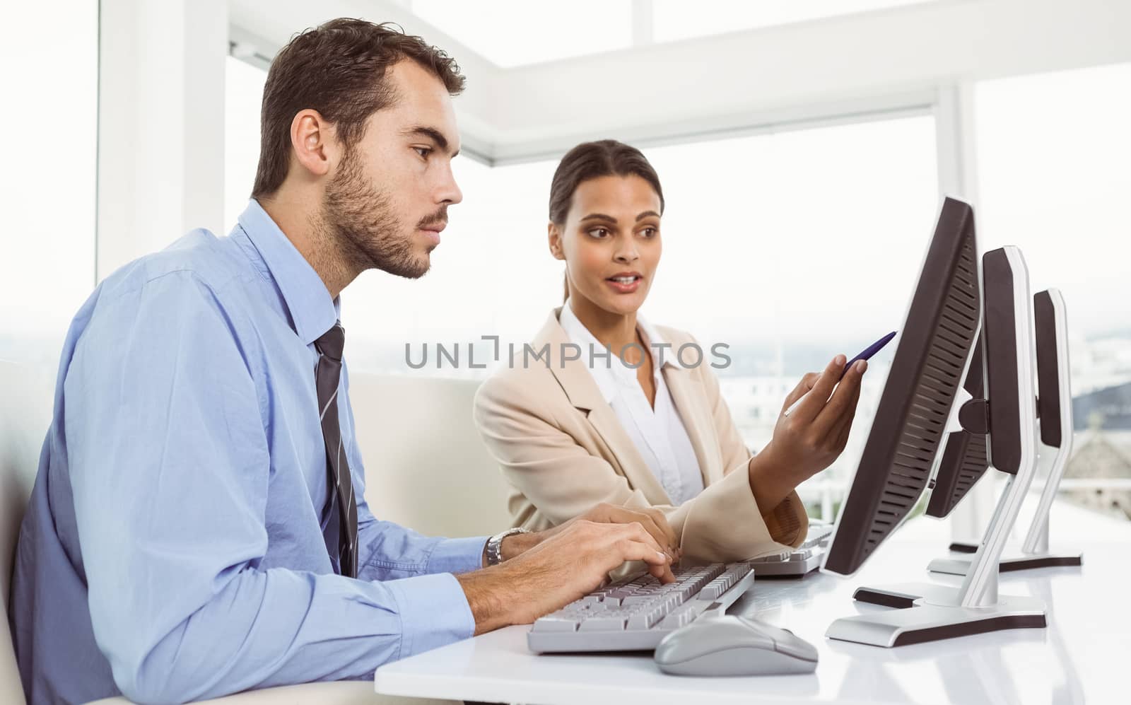 Two young business people using computer in office
