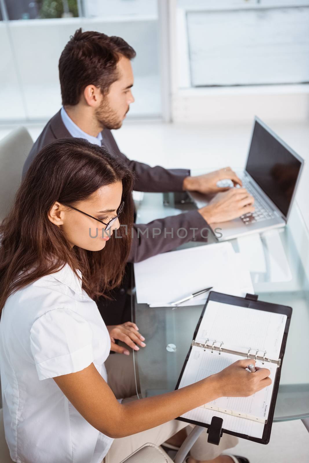 Two young business people with laptop and diary at office