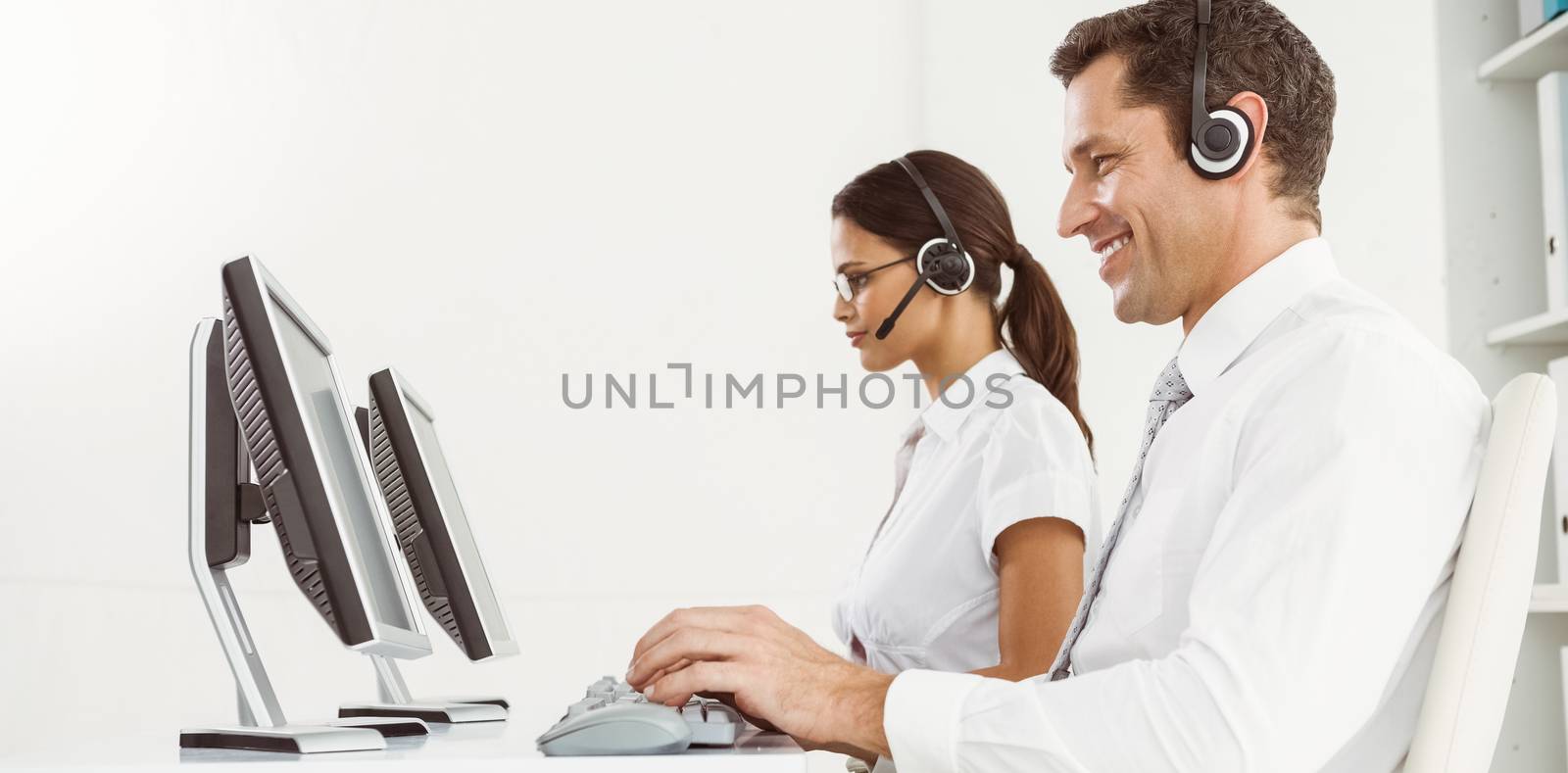 Side view of young business people with headsets using computers in office