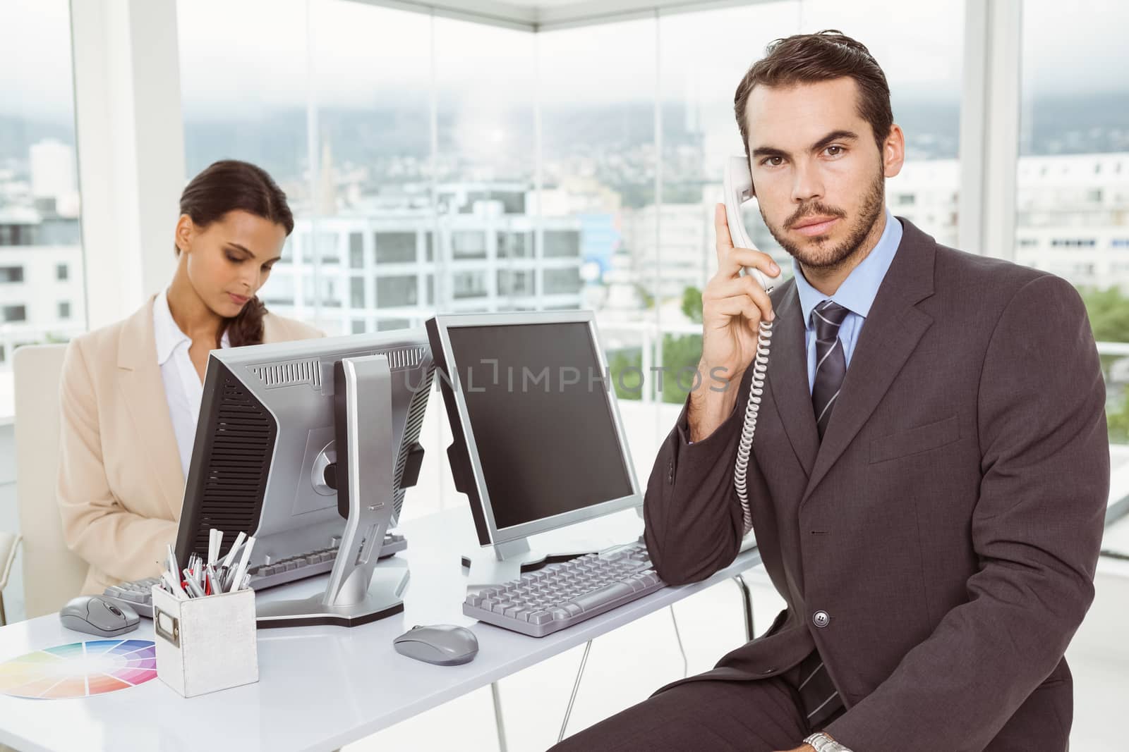 Two young business people using computers in office