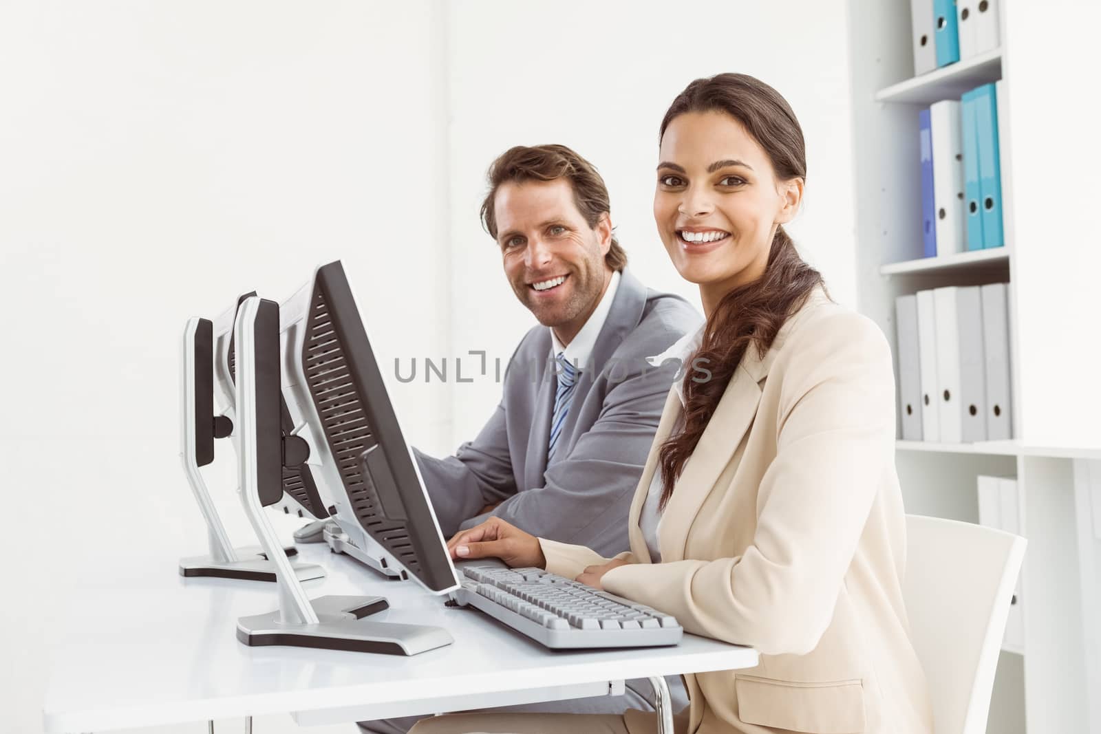 Two young business people using computers in office
