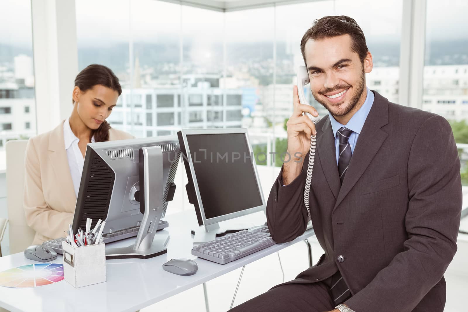 Two young business people using computers in office