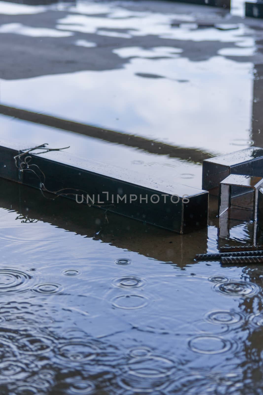 Big square metal pipes parts under rain on construction with sky in reflection. by alexsdriver