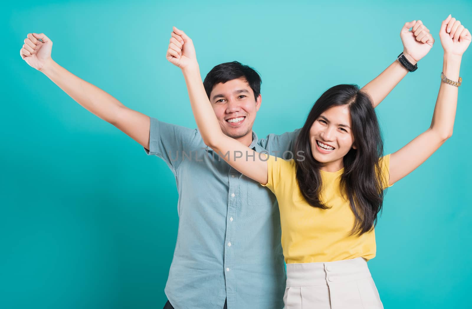 Portrait happy Asian young handsome man, beautiful woman excited funny couple smile standing so happy notices something unexpected and raised hands, studio shot on blue background