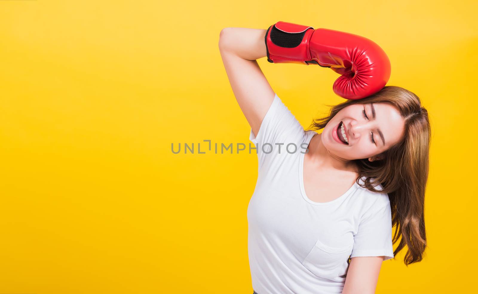 Portrait Asian Thai beautiful young woman standing smile in red boxing gloves punch head and close eyes, shoot the photo in studio shot isolated on yellow background, There was copy space for text