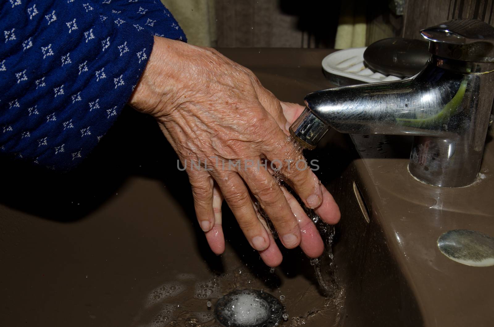 Older woman washing her hands to prevent coronavirus by VictorSuarez