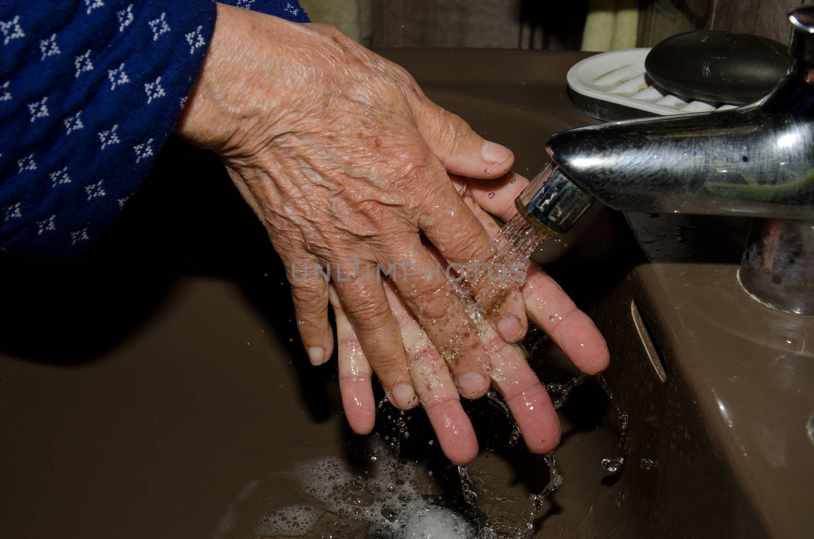 Older woman washing her hands to prevent coronavirus by VictorSuarez