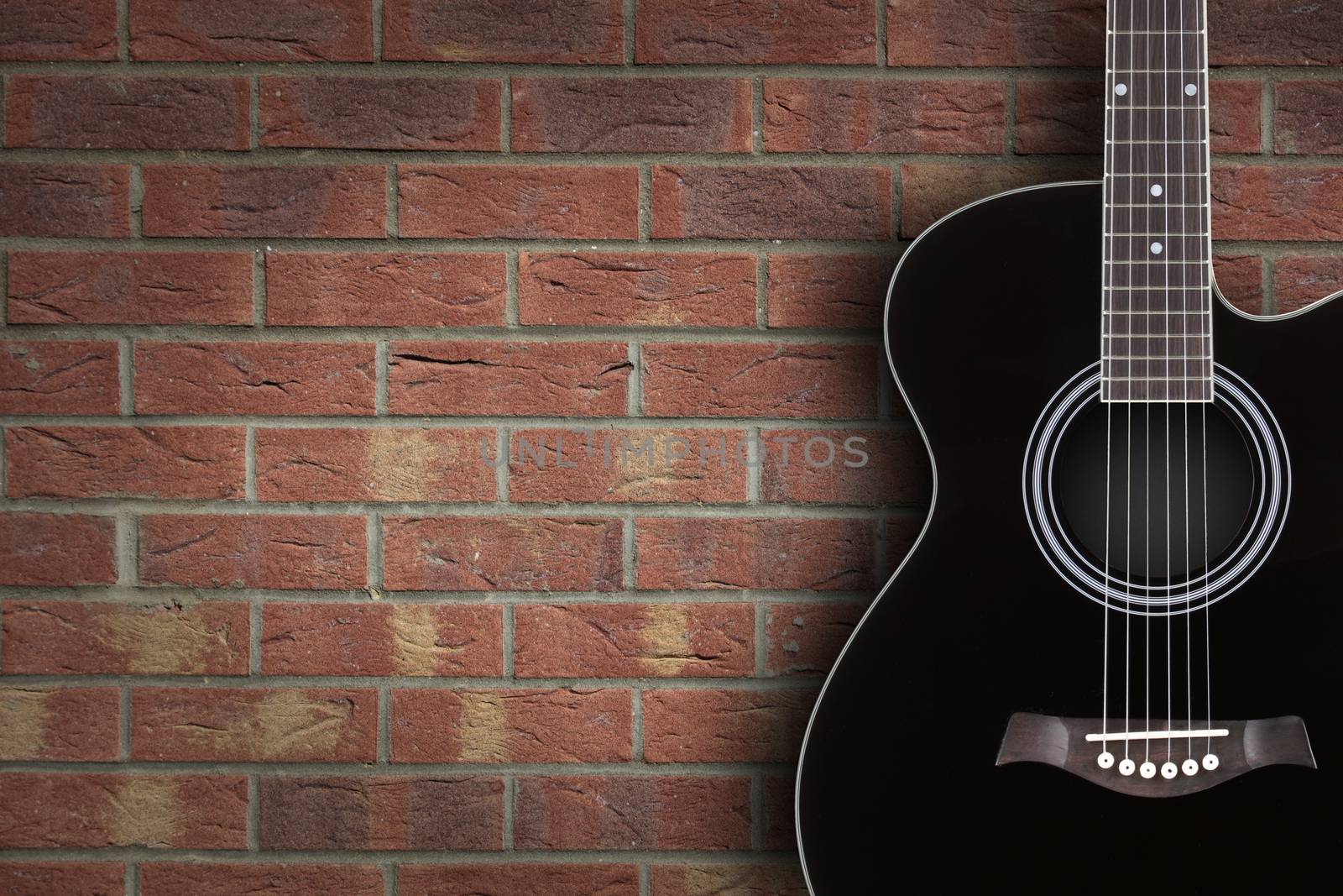 A black acoustic guitar on brick background with copy space