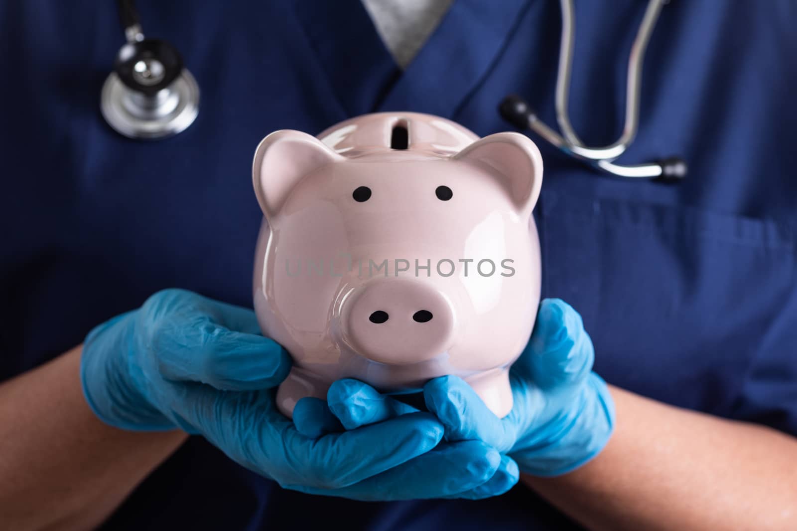 Doctor or Nurse Wearing Surgical Gloves Holding Piggy Bank.