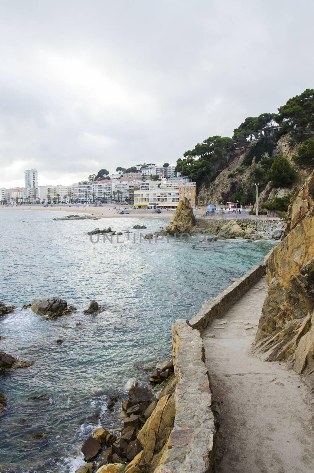 Panorama of Rocks and road near the coast of Lloret de Mar in a beautiful summer day and city on background, Costa Brava, Catalonia, Spain. Waterfront of the mountains in Mediterranean sea