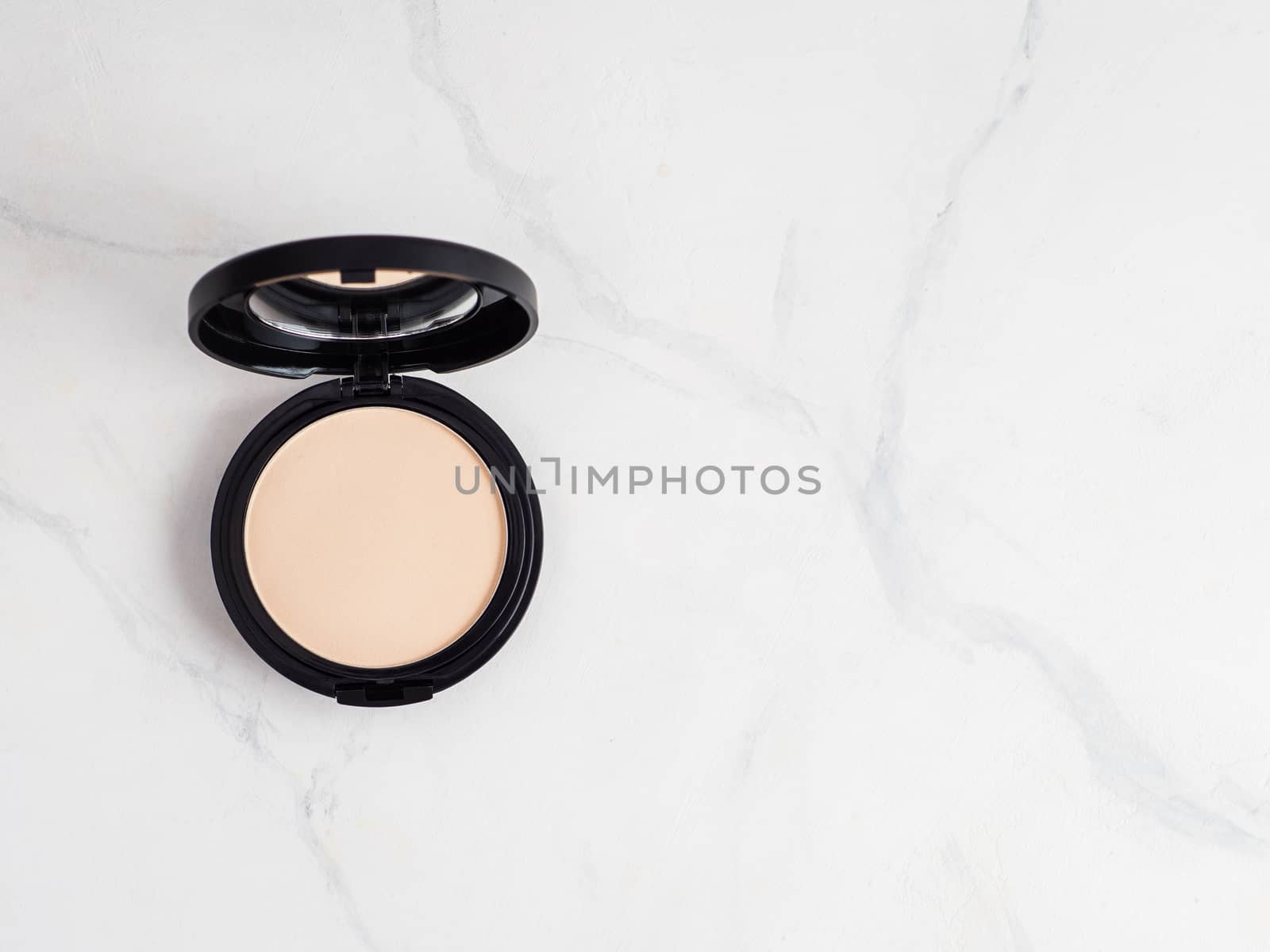 Compact powder on white marble background. Female pressed powder in opened black plastic case with mirror, copy space for text or design. Top view or flat lay