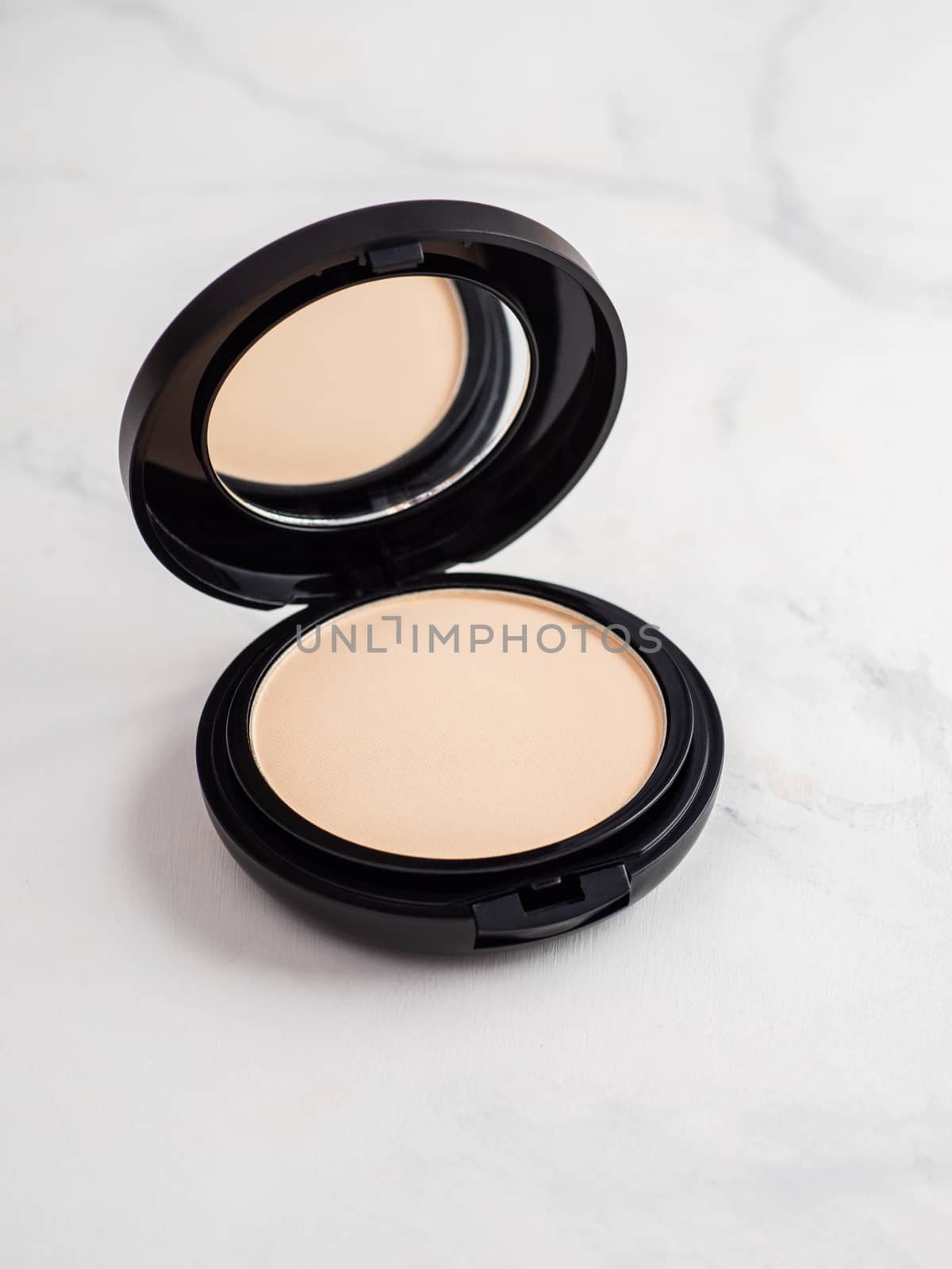 Compact powder on white marble background. Female pressed powder in opened black plastic case with mirror, copy space for text or design.
