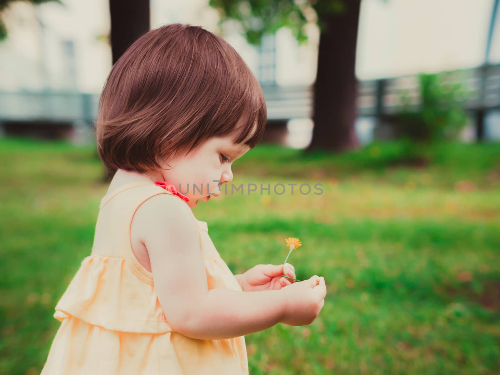 Little Baby Girl Portrait in profile outdoor. Cute Child over nature background. Adorable one year old baby with flower in hands