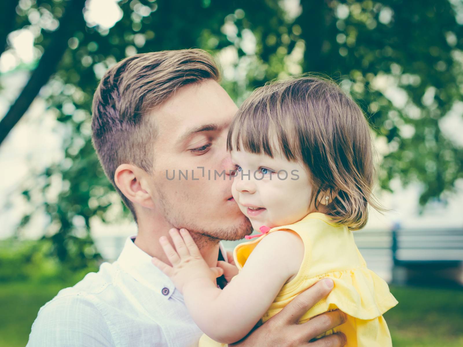 Close up of father holding his crying daughter. Dad kissing his little daughter