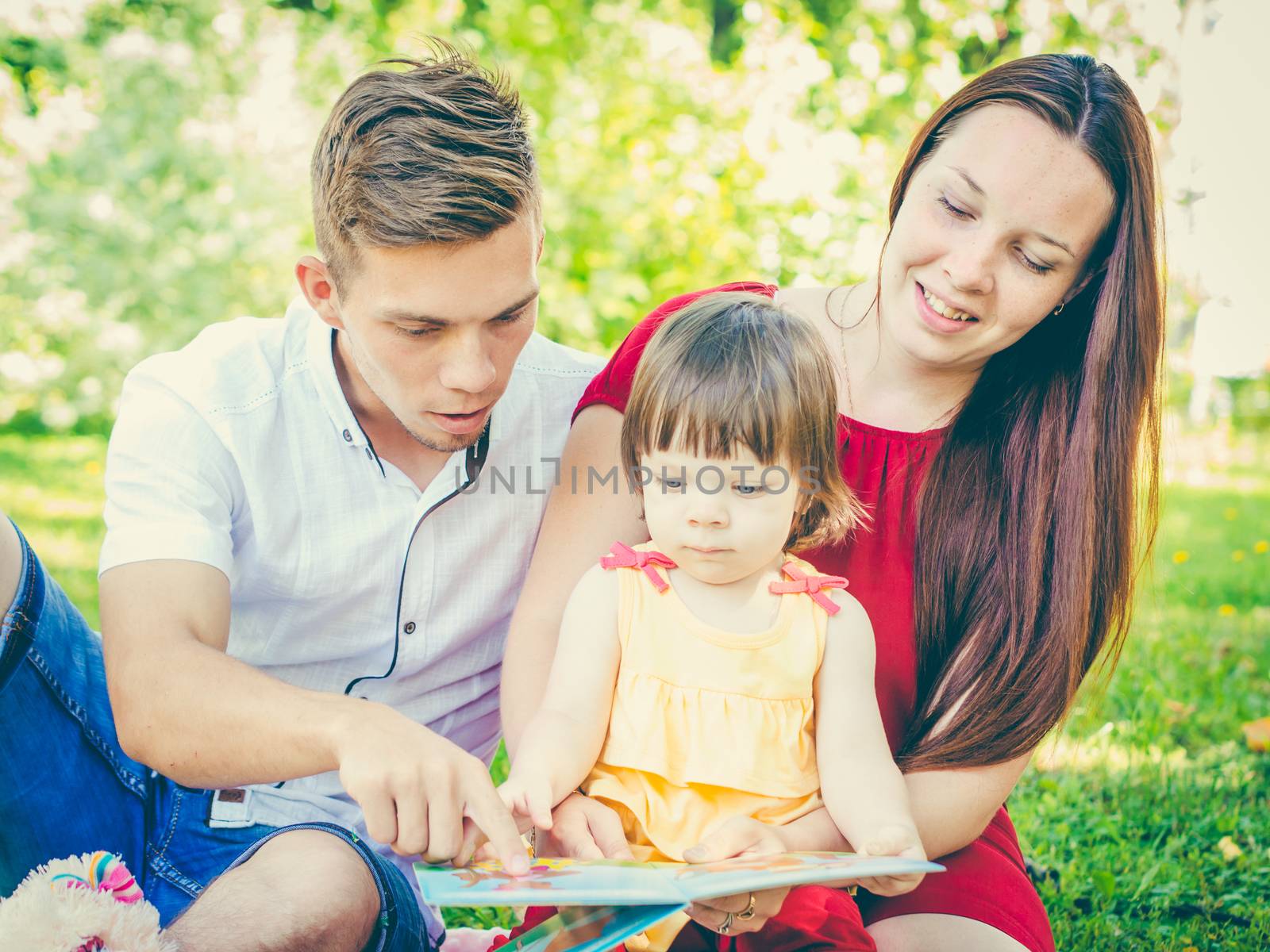 Parents and daughter reading book outdoors by fascinadora