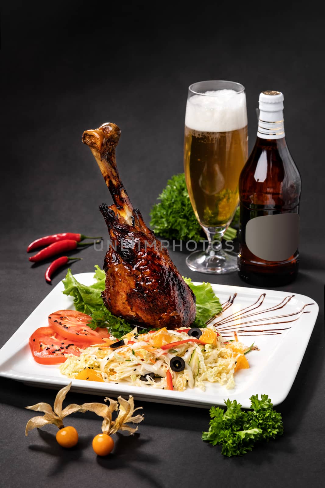 Lamb leg on a plate next to a bottle of beer on a black background