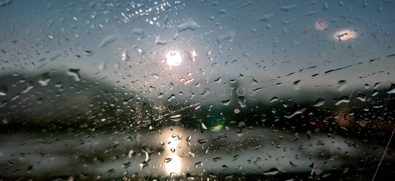 Raindrops on glass against rising sun and river.