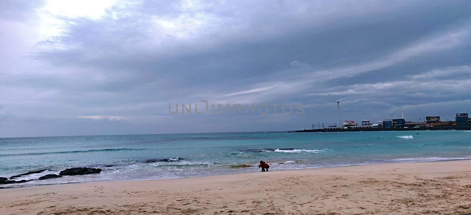 A child in red coat playing on the rocky beach during one cloudy evening