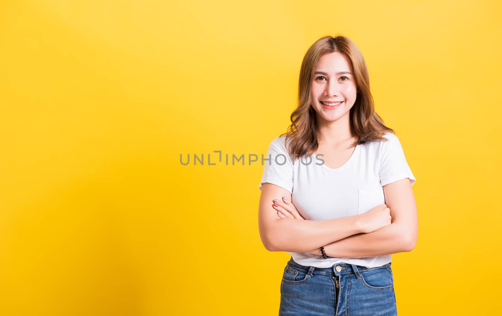 Asian Thai happy portrait beautiful cute young woman standing wear t-shirt her smile confidence with crossed arms looking to camera isolated, studio shot on a yellow background and copy space