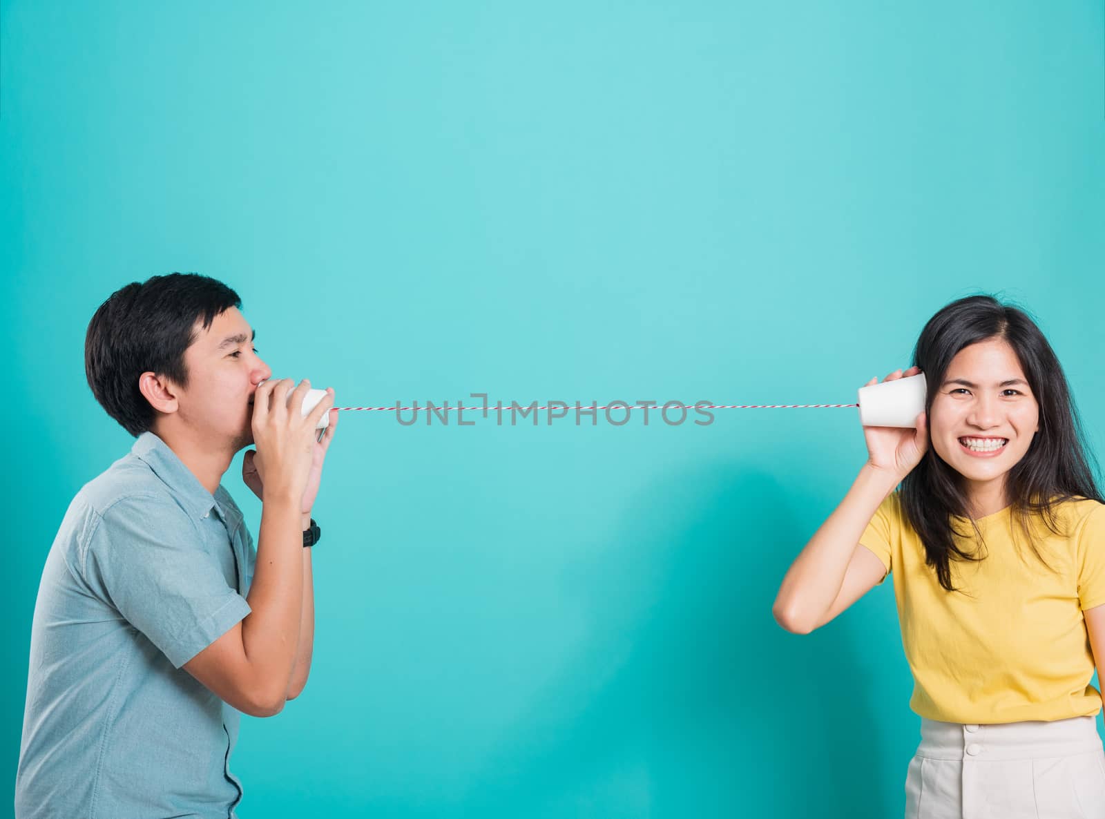 Asian happy young couple beautiful handsome smile and talking together with paper can telephone in a studio shot on blue background with copy space for text