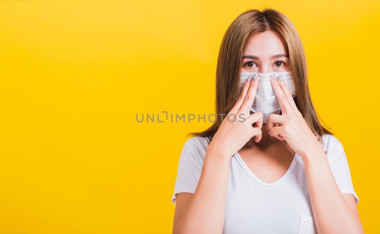 Portrait Asian beautiful young woman wearing face mask protect filter dust pm2.5 anti-pollution, anti-smog, COVID virus and air pollution her use hand bridge nose on yellow background, with copy space