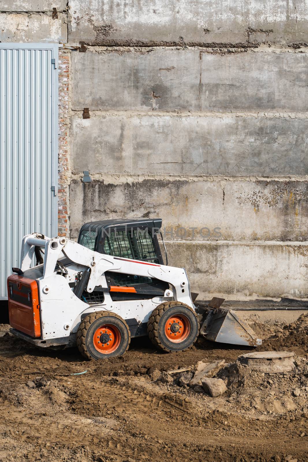 White skid steer loader at a construction site working with a soil. Industrial machinery. Industry