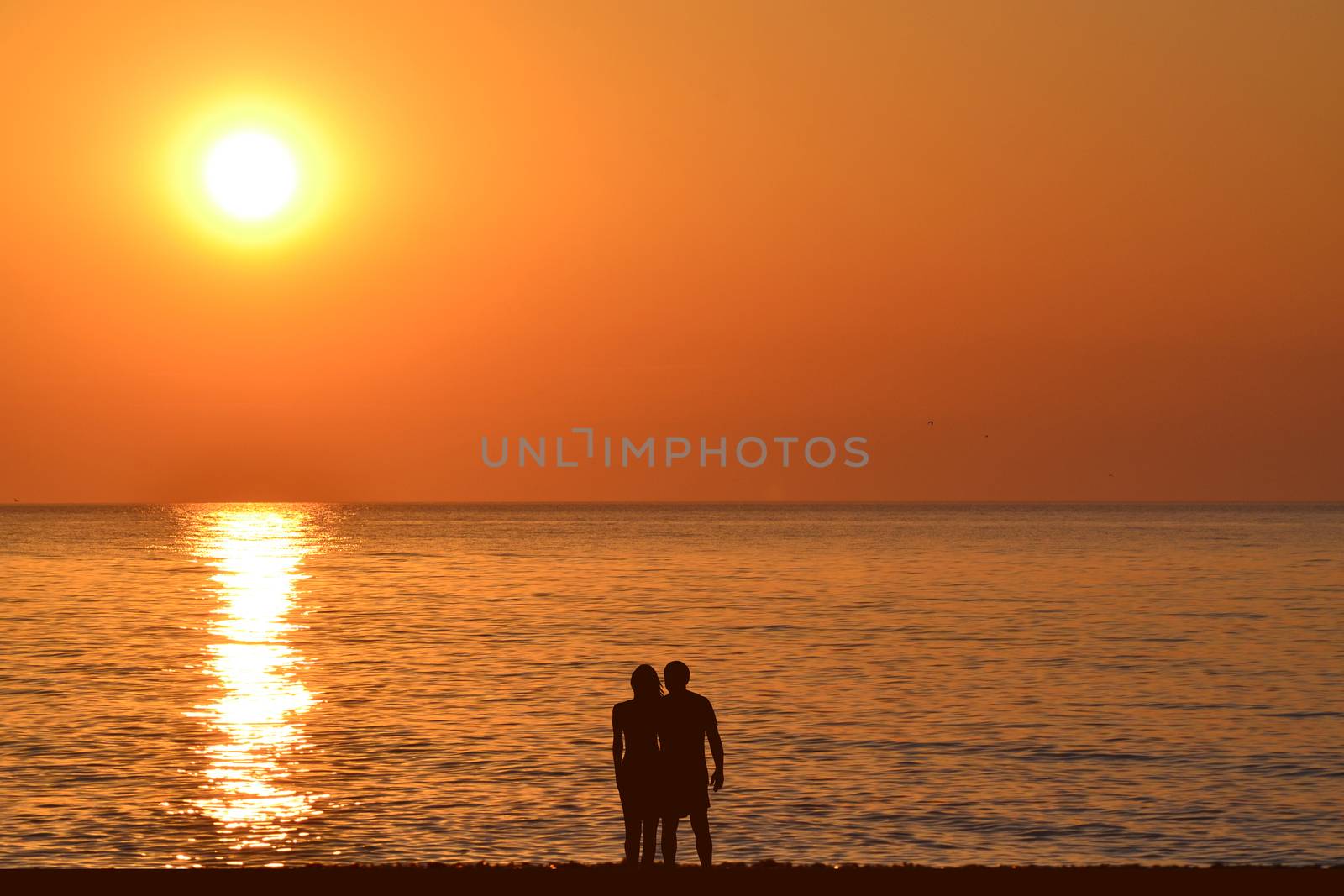 Silhouettes of romantic hugging couple on the beach at sunrise by hibrida13