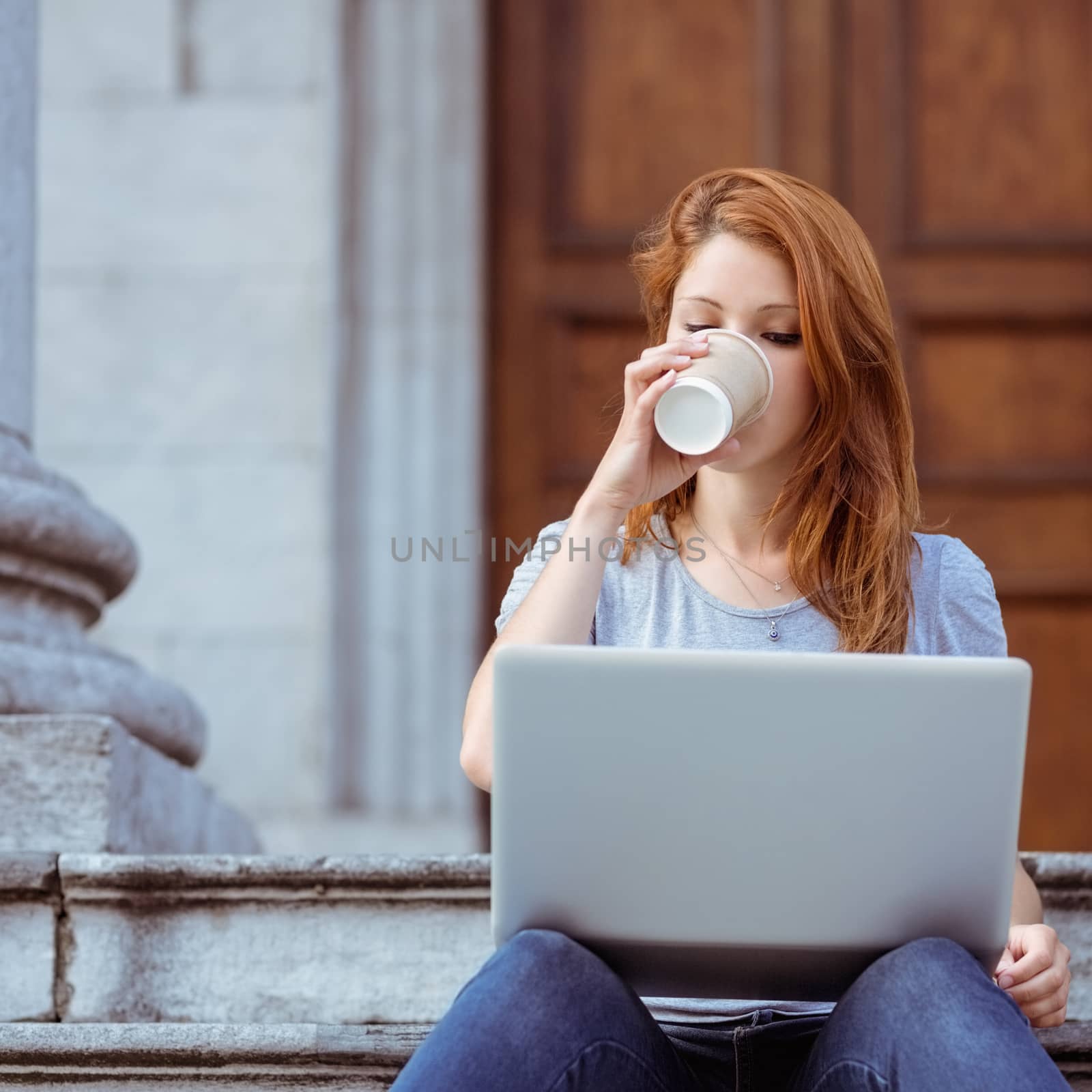 Beautiful woman drinking of disposable cup using her laptop in the street