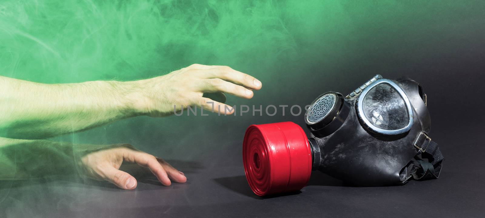 Man in room filled with smoke, trying to reach for vintage gasmask - Isolated on black - Green smoke