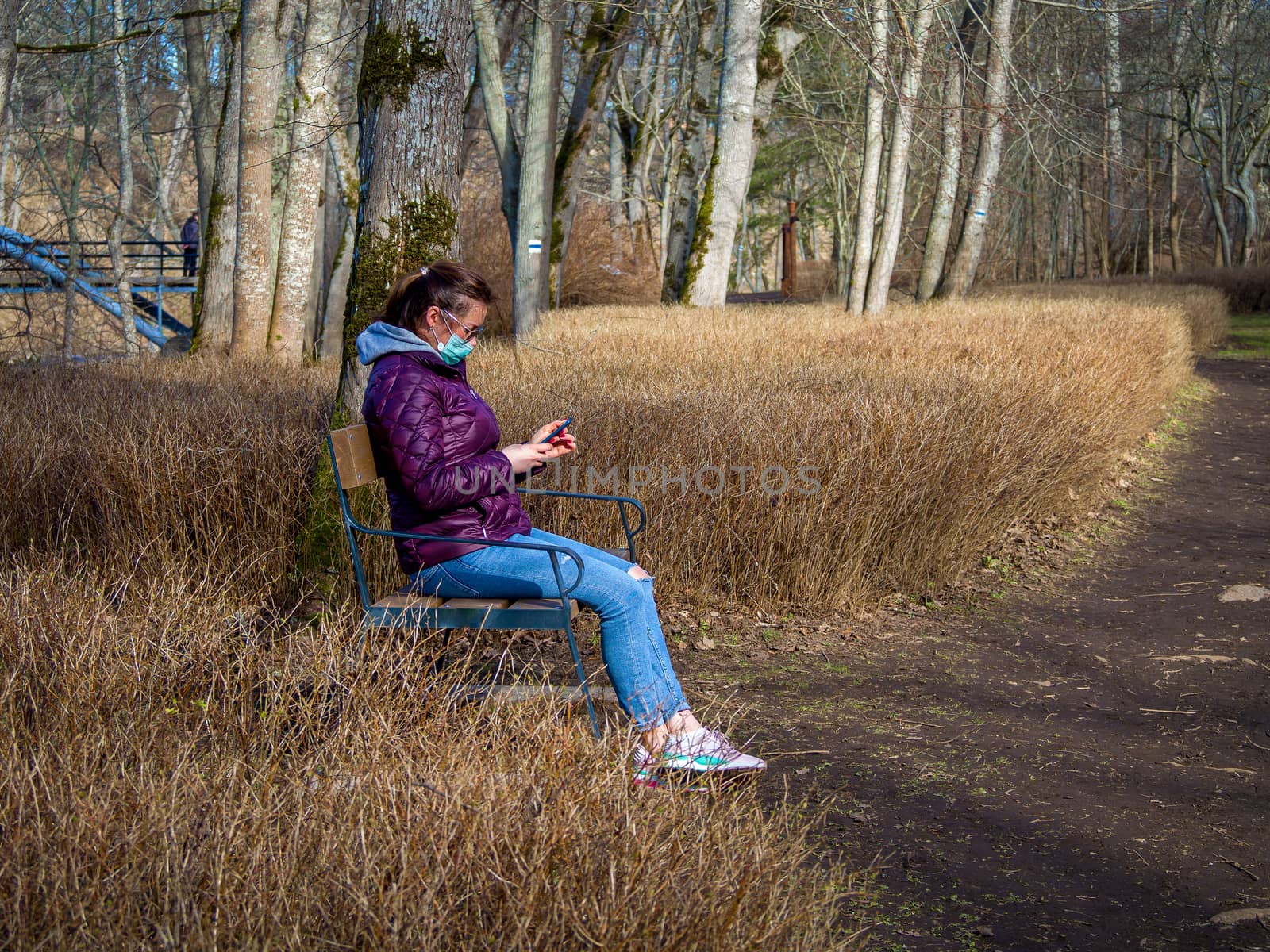 Lady and coronavirus protection. Sad Woman sitting alone on bench in park wearing mask to avoid infectious. Corona virus, or Covid 19, is spreading all over the world. Receives bad news on her phone.