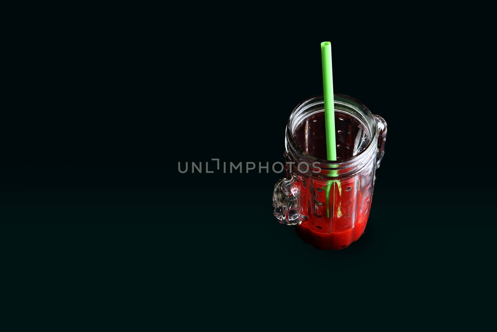 glass of tomato juice in with a green straw with a black background