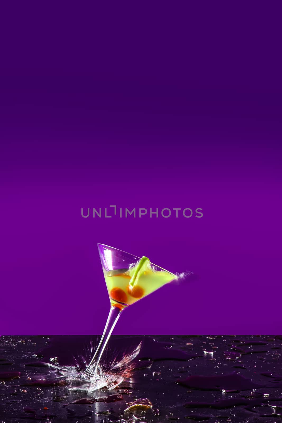 New Years concept of a crashing alcohol glass with purple background and yellow drink