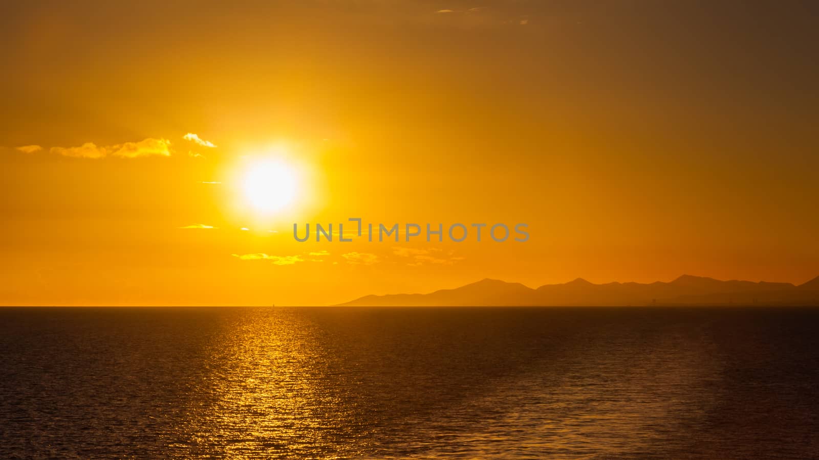 Sunset over the coastline of the Spanish Canary island of Lanzarote.  A yacht can be seen passing under the sun on the horizon.