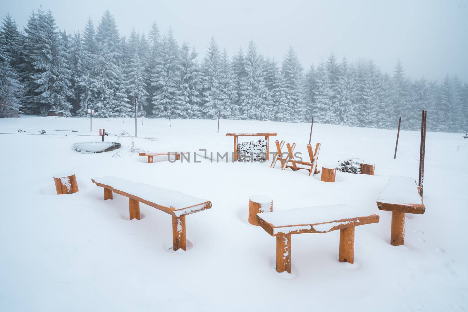 Winter forest camp, woden benches and fireplace covered in snow, snowy landscape.