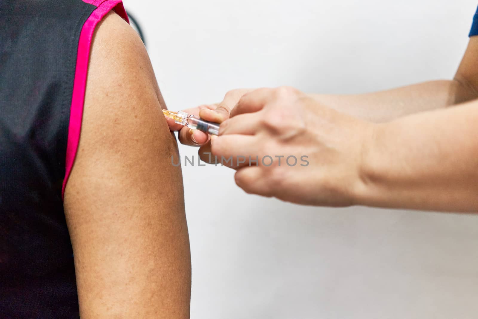 Hand of nurse holding hypodermic syringe is injecting vaccine of flu with left shoulder of man in black sleeveless sports shirt. Close up shoulder of man. Healthcare and medical concept photography.