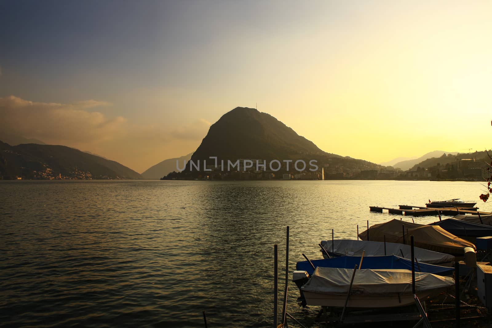 Water front with view of Lugano city and lake, Switzerland, with lake and mountains during sunset