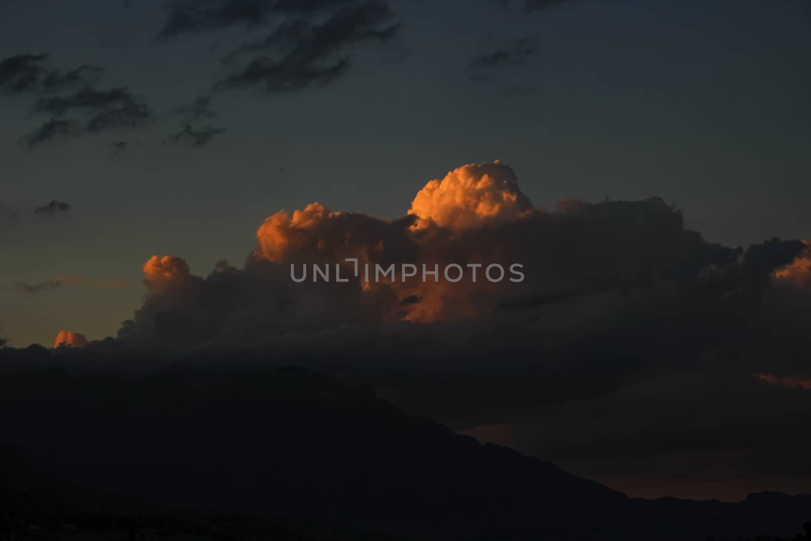 dark sky with orange storm clouds over mountain range, with dramatic clouds