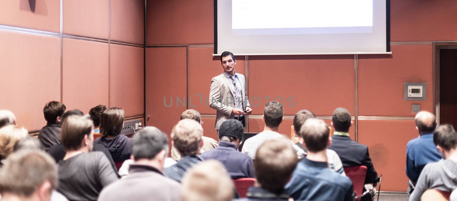 Speaker giving a talk in conference hall at business meeting event. Rear view of unrecognizable people in audience at the conference hall. Business and entrepreneurship concept.